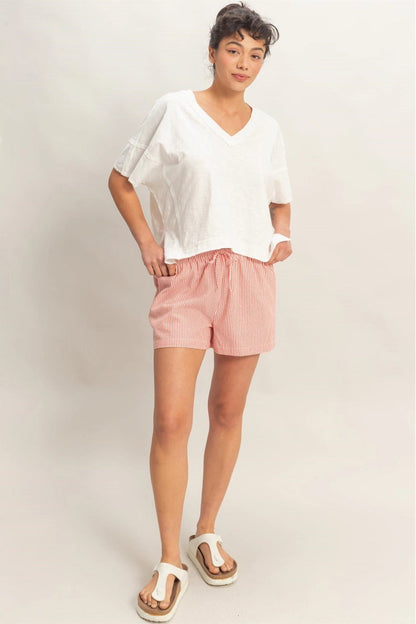 Woman wearing a white top and pink shorts against a plain background