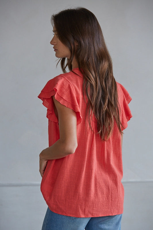 Woman wearing a coral ruffled blouse against a plain background