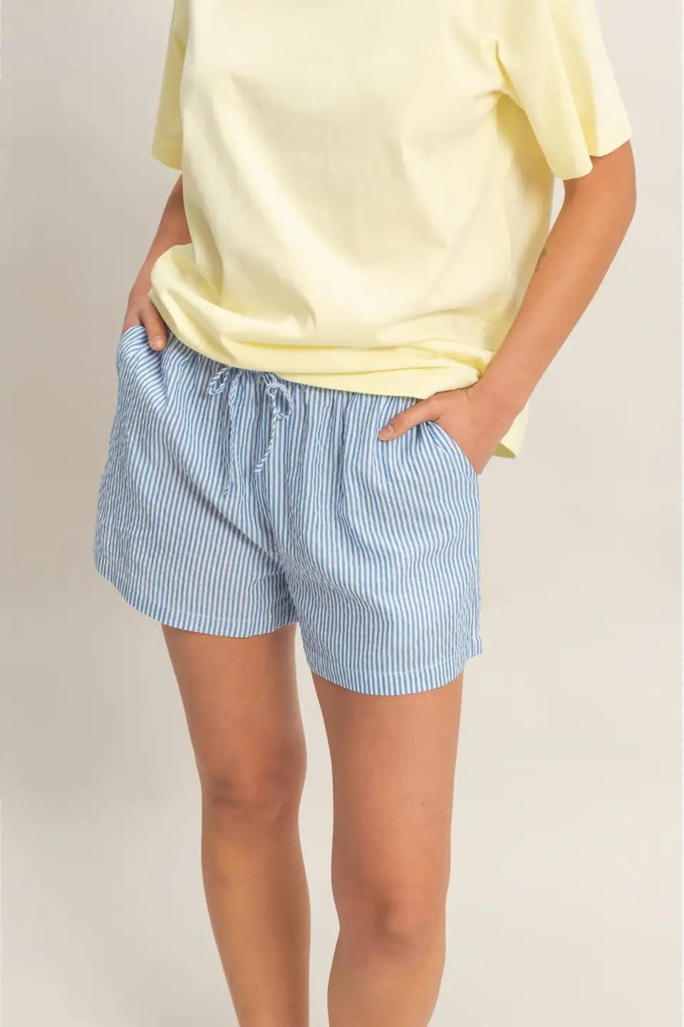 Person wearing light yellow top and blue striped shorts on a plain background