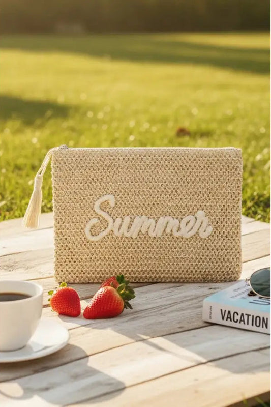 Woven clutch bag with 'Summer' text on a wooden table outdoors.