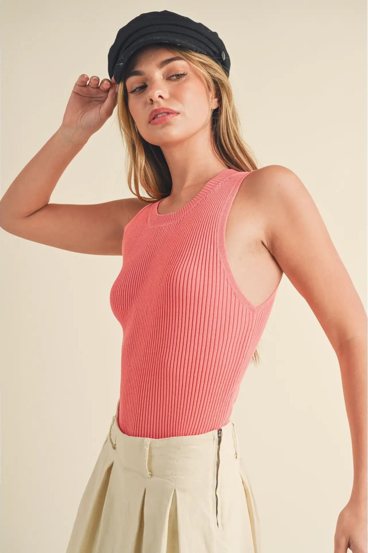 Woman wearing a pink ribbed tank top and beige cap against a beige background