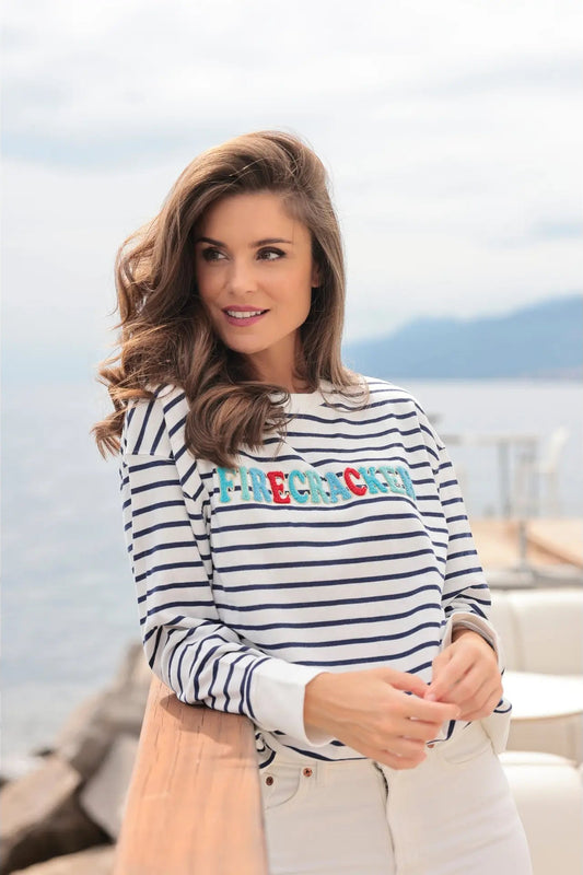 Woman wearing a striped shirt with colorful text, standing by a body of water.