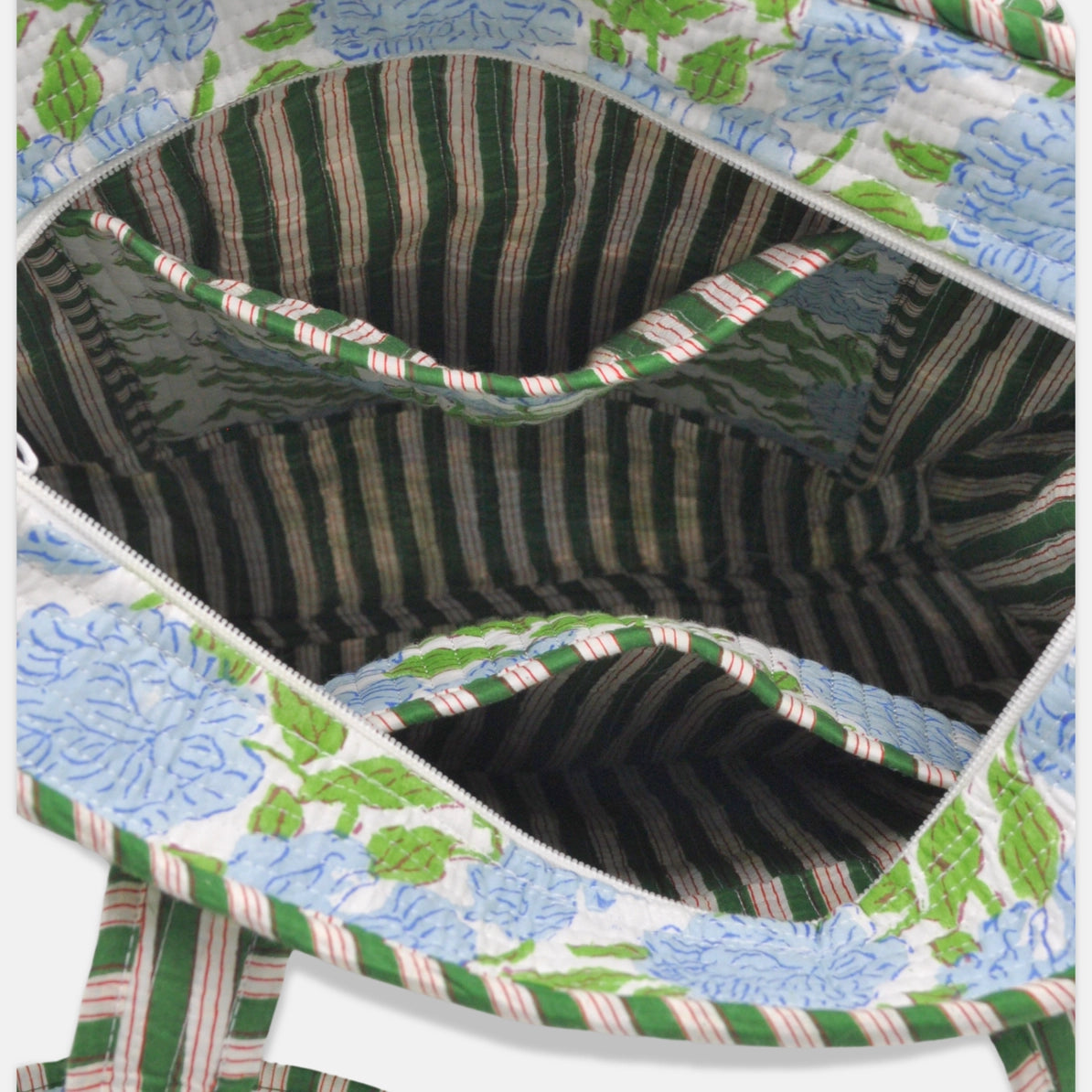 Close-up of the interior of a quilted tote bag, showing a striped green and beige lining with a floral exterior pattern in light blue and green on a white background.