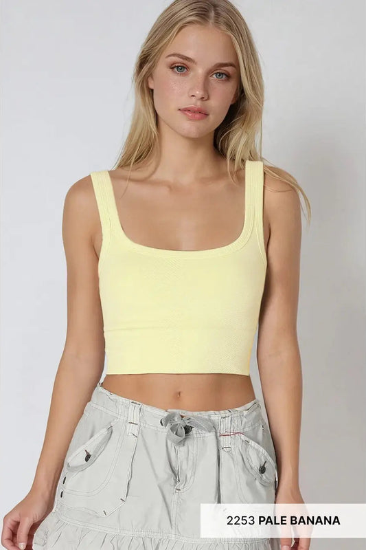 Woman wearing a light yellow tank top and light gray pants on a white background