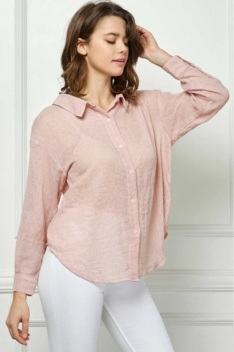 Woman wearing a light pink button-up shirt and white pants in a minimalistic setting