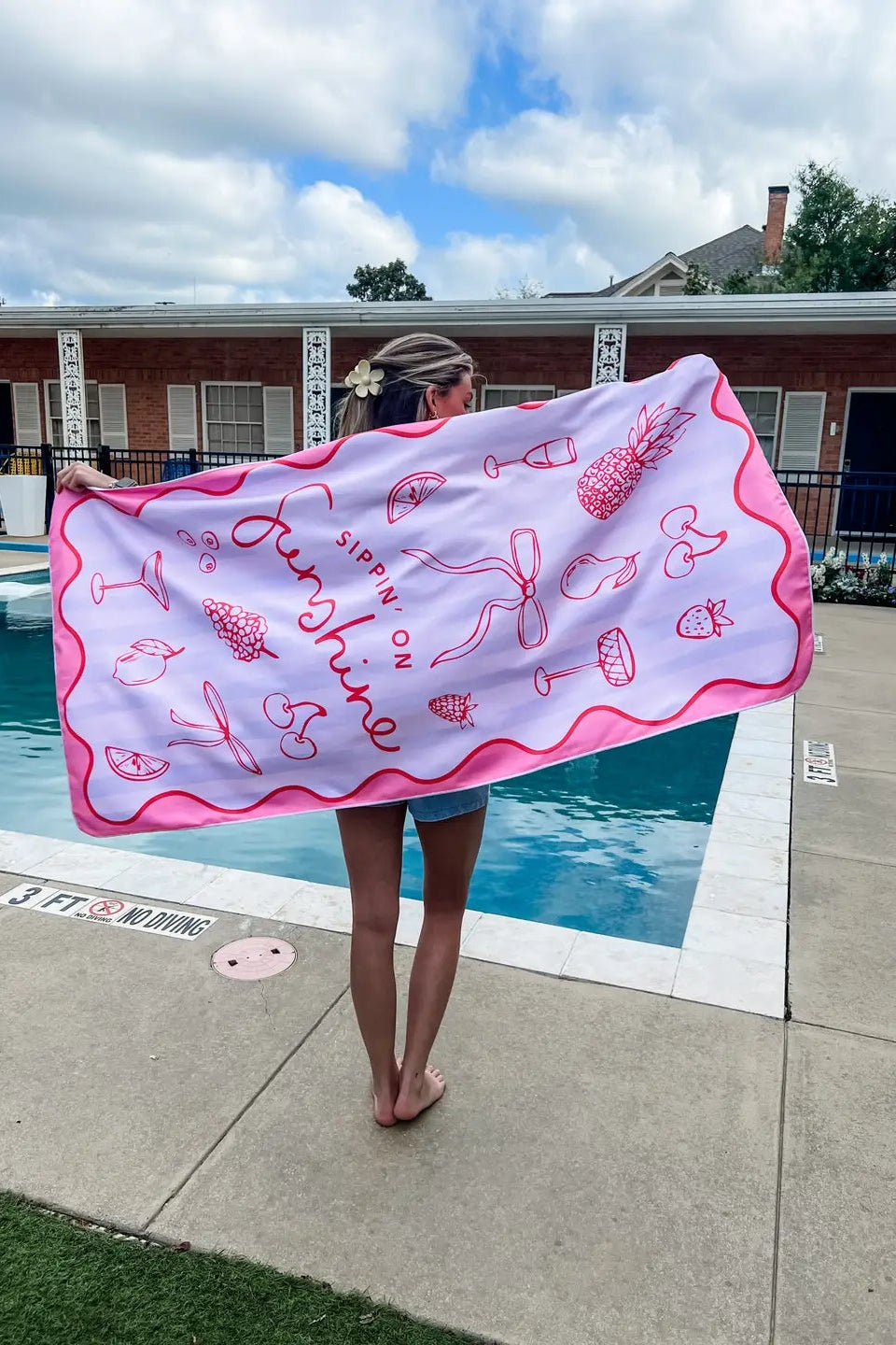 Person holding a pink towel with graphics by a poolside