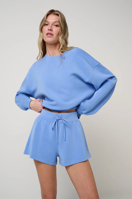 Woman wearing a blue outfit with a sweater and shorts on a plain background