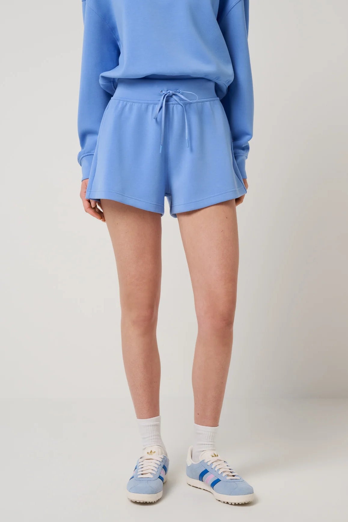 Person wearing a blue tracksuit with shorts on a plain background