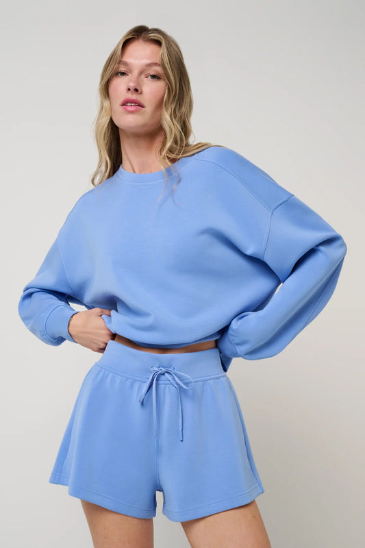 Woman wearing a blue outfit with a matching sweater and shorts on a plain background