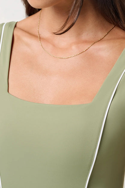 Close-up of a person wearing a green tank top with white trim and a gold necklace.