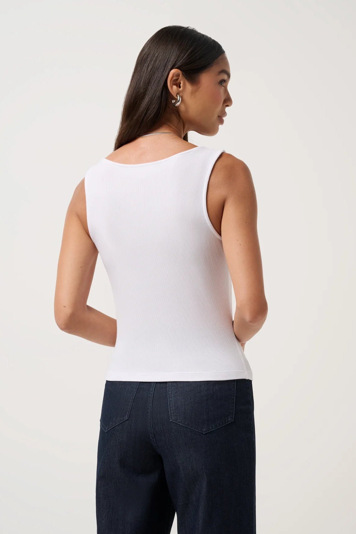 Woman wearing a white sleeveless top and dark pants on a light background