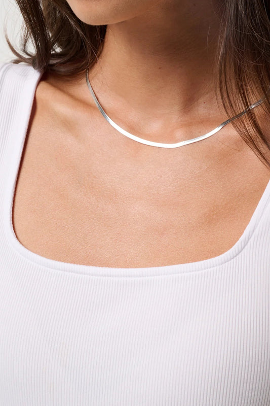 Silver necklace on a person wearing a white tank top against a neutral background