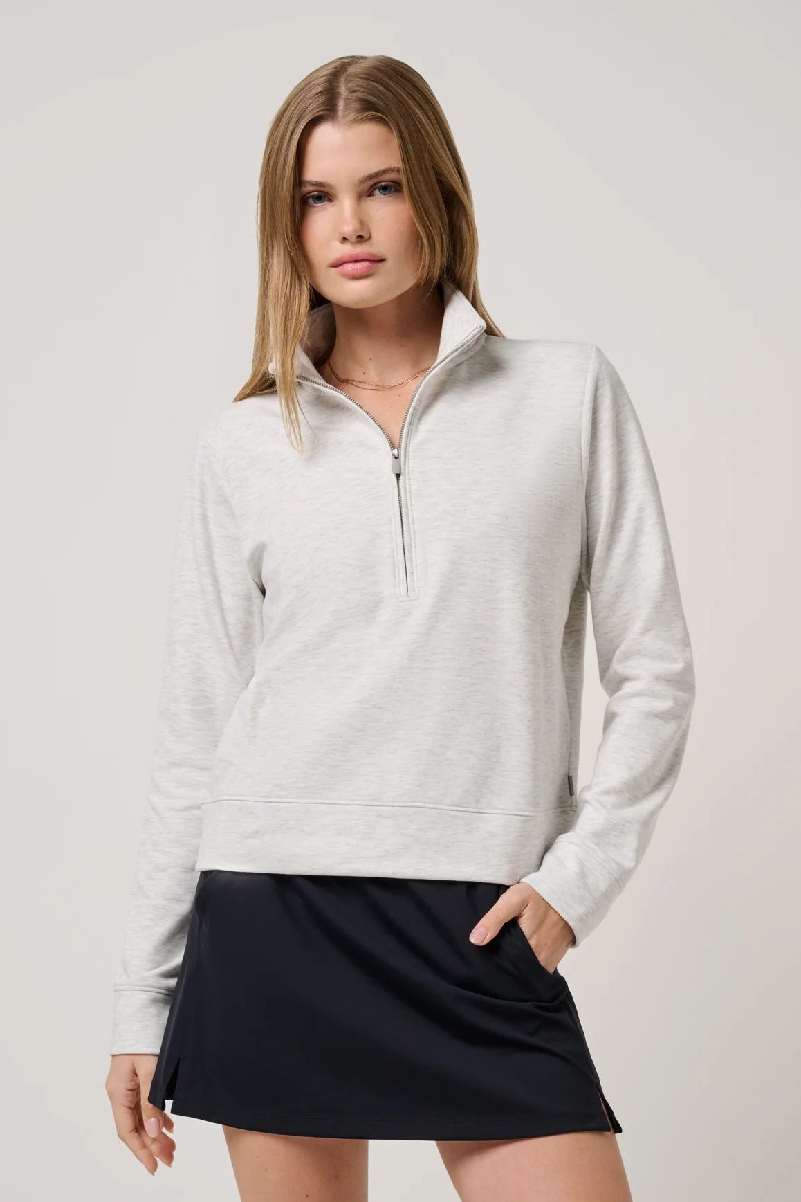 A woman modeling a light heather gray quarter-zip pullover sweater paired with a dark navy mini skirt, set against a plain light gray studio background.