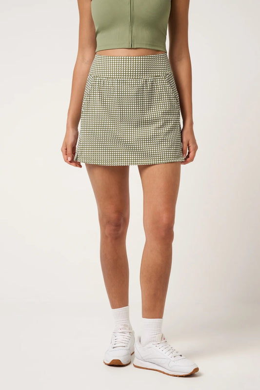 Person wearing a green checkered skirt and white sneakers on a plain background