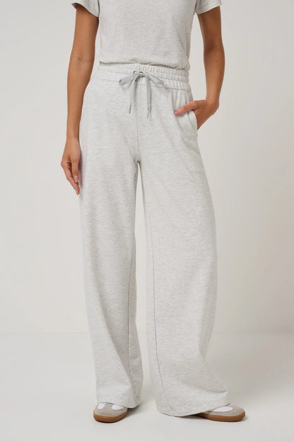 A person wearing light heather gray wide-leg sweatpants with an elastic drawstring waist, paired with a matching light gray top and beige sandals, shown against a plain light gray studio background.
