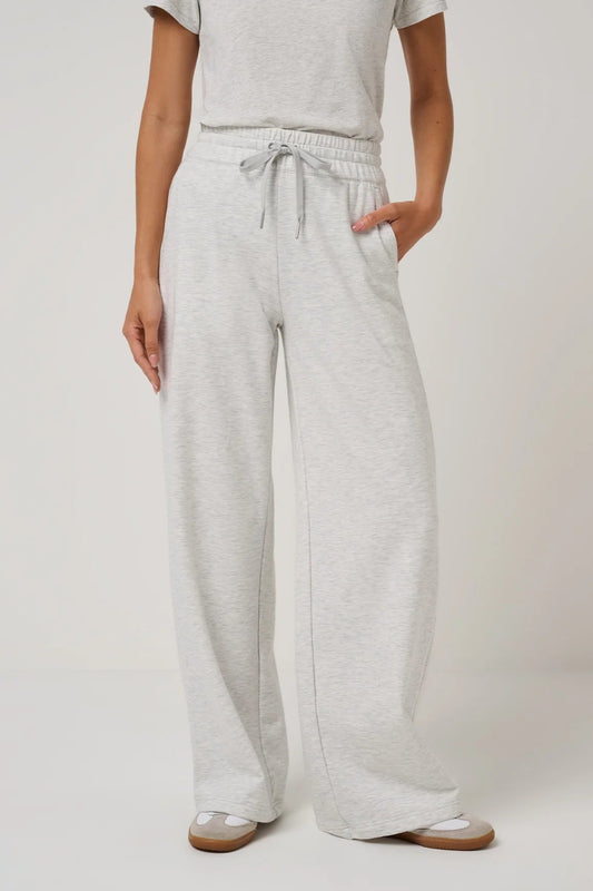 A person wearing light heather gray wide-leg sweatpants with an elastic drawstring waist, paired with a matching light gray top and beige sandals, shown against a plain light gray studio background.