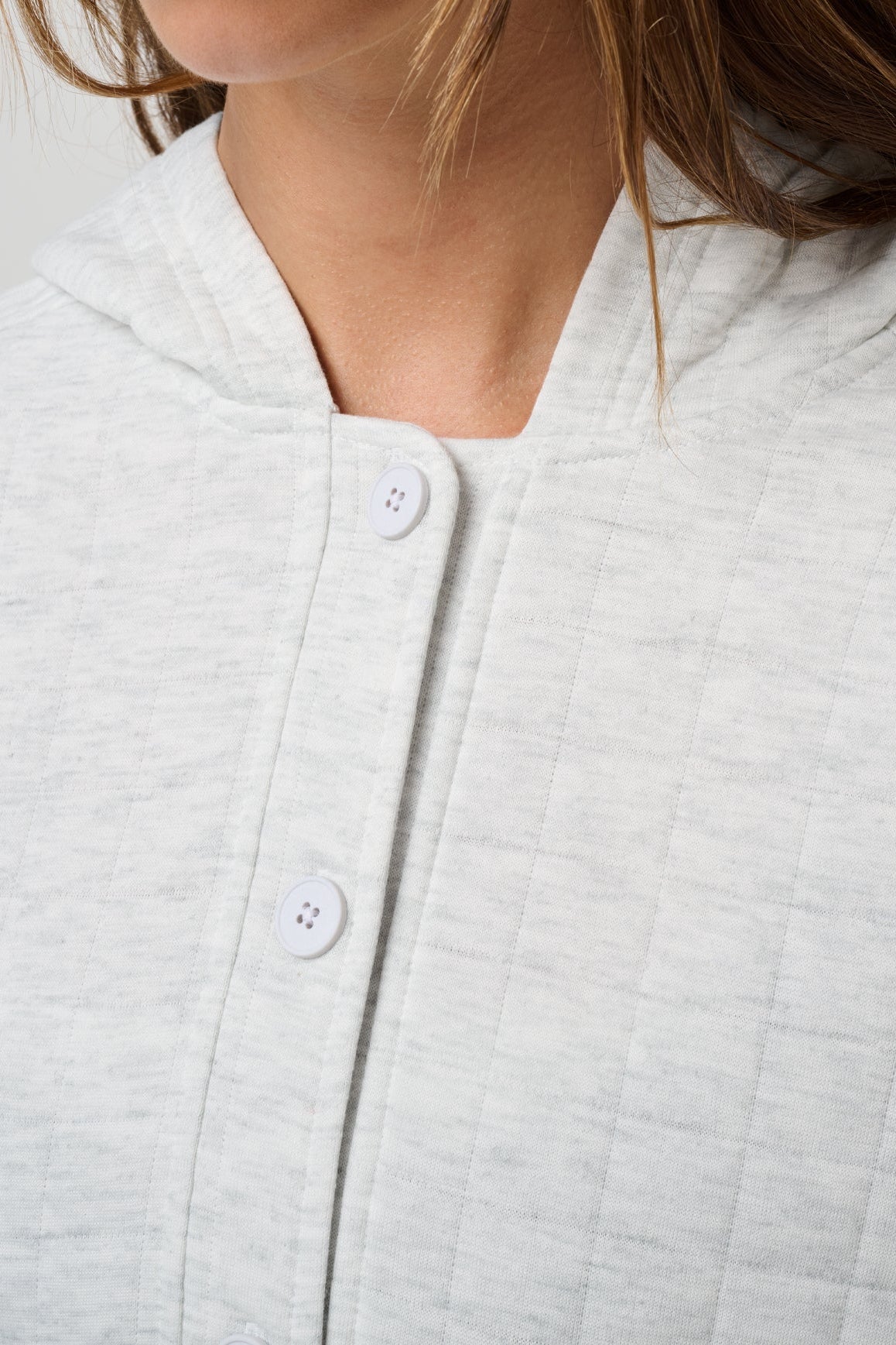 Close-up of a light heather gray quilted top with a split neckline and white buttons, worn by a model.