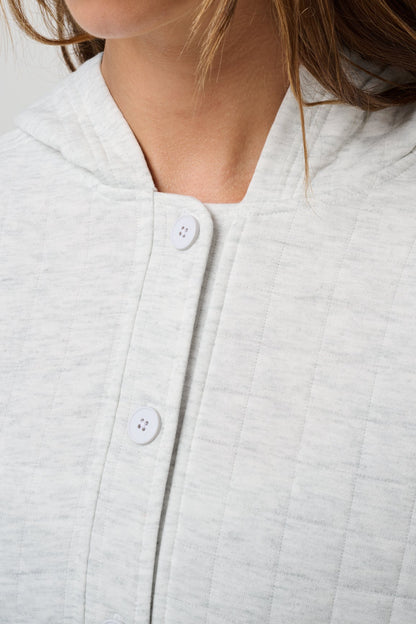 Close-up of a light heather gray quilted top with a split neckline and white buttons, worn by a model.