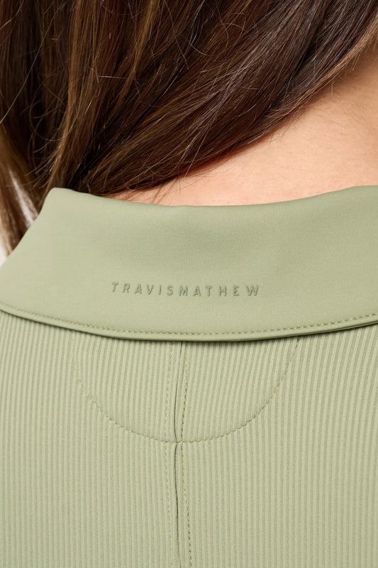 Close-up of a green jacket collar with 'Travis Mathew' branding.