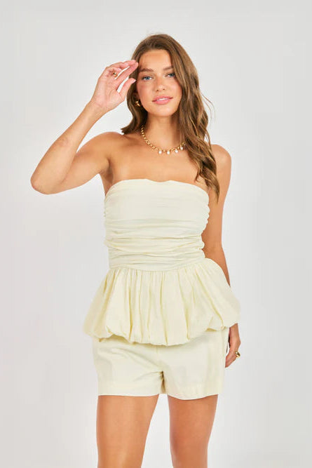Woman wearing a light yellow strapless top and shorts set on a white background