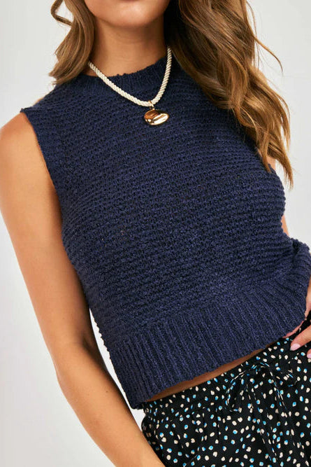 Woman wearing a navy blue sleeveless knitted top with a plain background