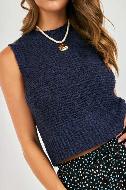 Woman wearing a navy blue sleeveless knitted top with a plain background