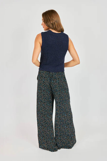 Woman wearing a navy sleeveless top and patterned pants on a light gray background