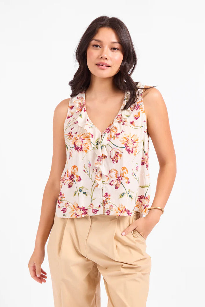 Woman wearing a floral sleeveless top and beige pants on a white background