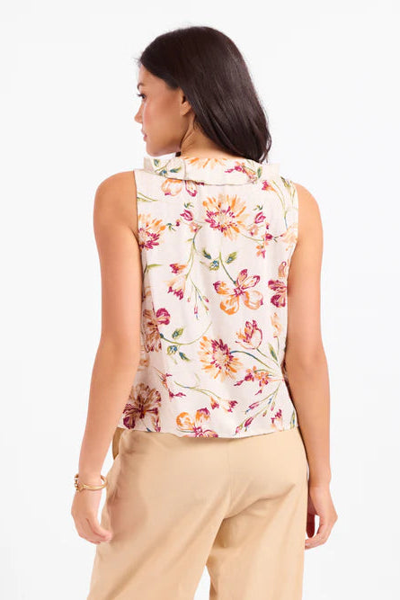 Woman wearing a sleeveless floral top and beige pants on a white background