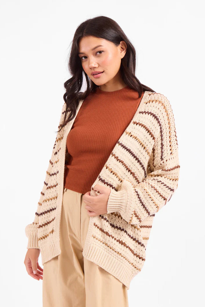 Woman wearing a beige cardigan with brown stripes, brown top, and beige pants on a white background