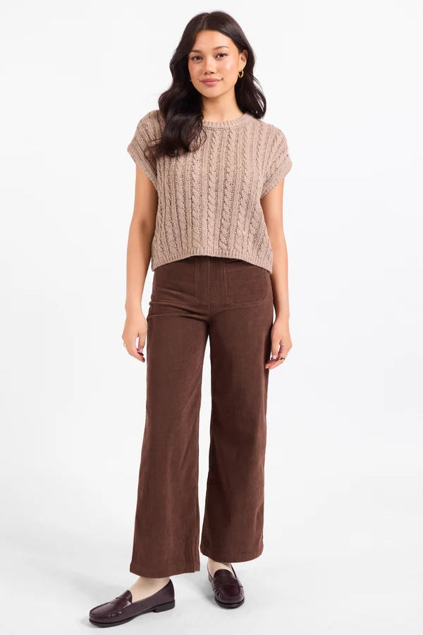 A woman modeling a short-sleeve beige cable-knit cropped sweater and brown wide-leg corduroy pants, paired with dark brown loafers, against a plain white studio background.