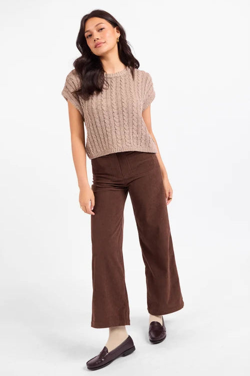 A woman modeling a beige cable-knit short-sleeve crop top and brown wide-leg corduroy pants against a plain white studio background.