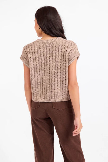 Woman wearing a beige knitted top and brown pants on a white background