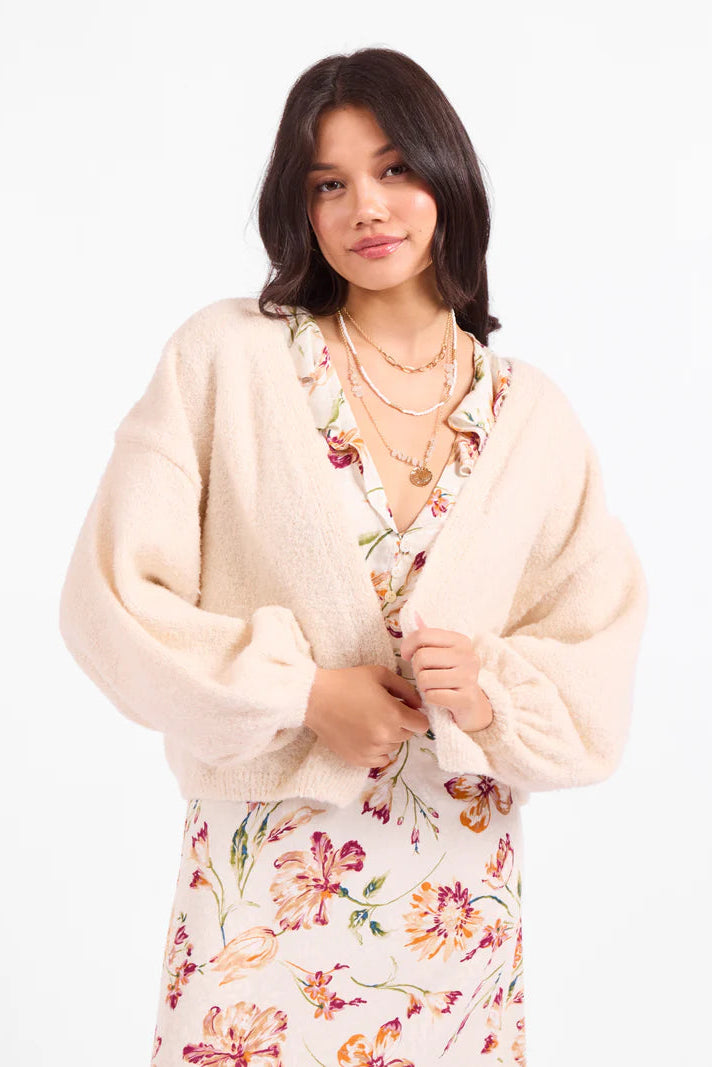 Woman wearing a floral dress and cream cardigan on a white background