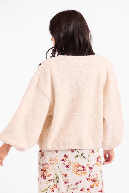 Woman wearing a light pink sweater over a floral dress on a white background