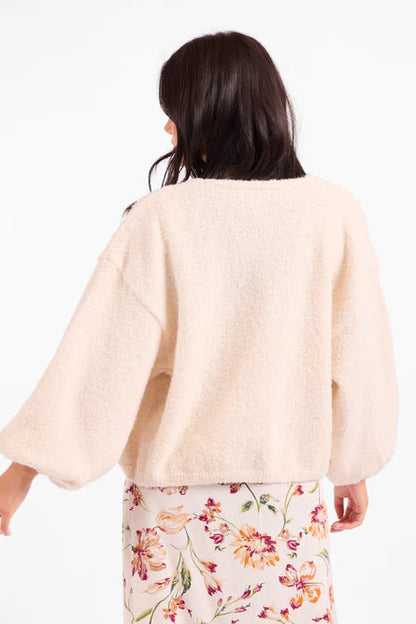 Woman wearing a light pink sweater over a floral dress on a white background