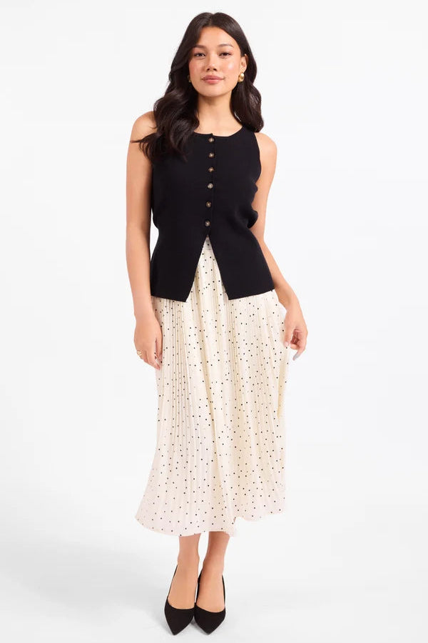 A woman modeling a sleeveless black vest with a button front and a long cream skirt with a small floral print, standing against a plain white studio background.