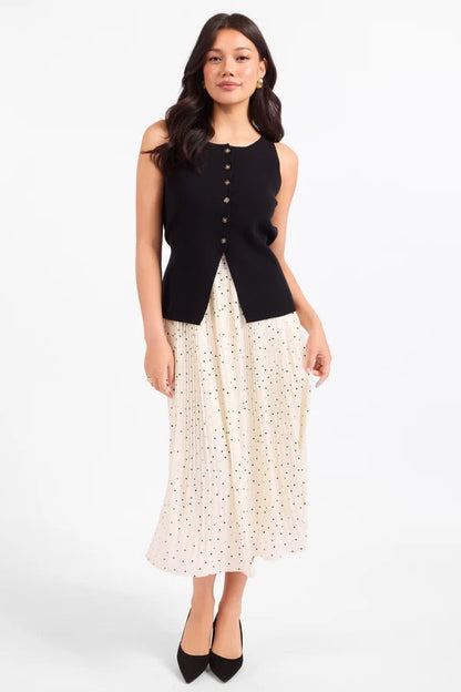 A woman modeling a sleeveless black vest with a button front and a long cream skirt with a small floral print, standing against a plain white studio background.