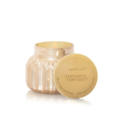 A capri BLUE Candle in a faceted gold glass jar with its lid leaning against it, on a clean white background.