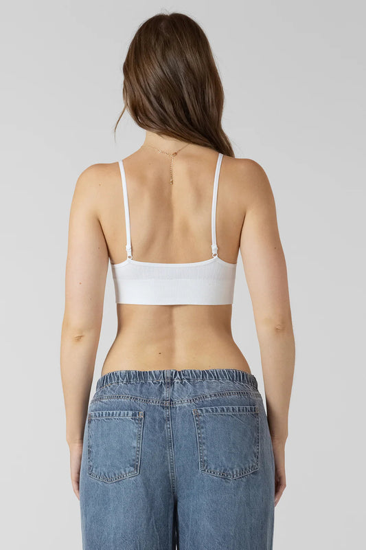 Woman wearing a white bralette and blue jeans on a plain background