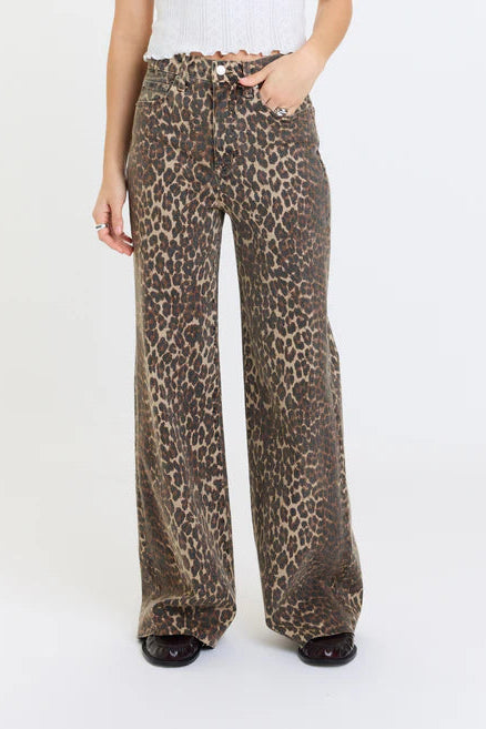 A person wearing high-waisted, wide-leg pants with an animal print pattern in brown, beige, and black, paired with a white ribbed top and black shoes, against a plain white studio background.