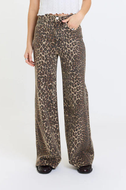A person wearing high-waisted, wide-leg pants with an animal print pattern in brown, beige, and black, paired with a white ribbed top and black shoes, against a plain white studio background.