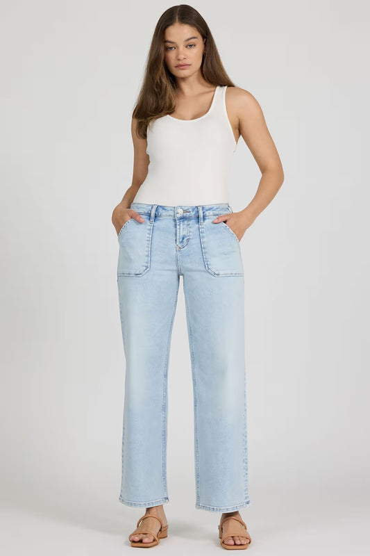 Woman wearing light blue jeans and a white tank top on a plain background