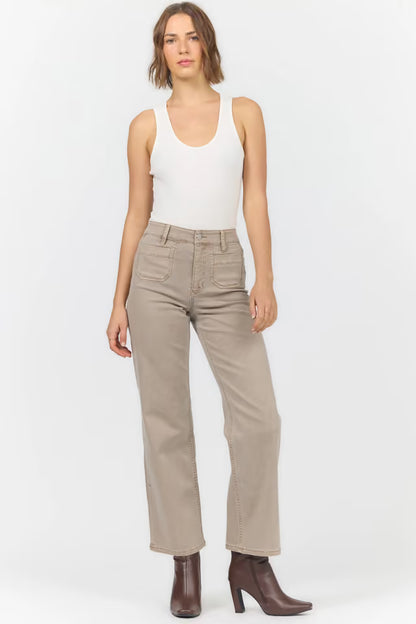 A model wearing beige straight-leg jeans, a white tank top, and brown ankle boots, standing against a light gray studio background.