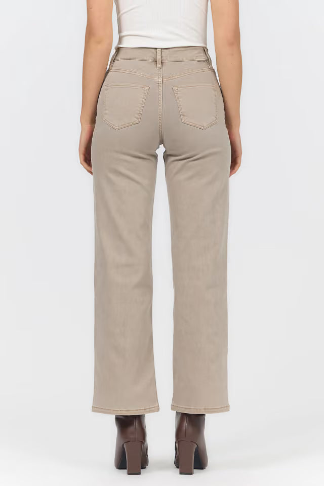 A person shown from the back wearing light beige straight-leg jeans with a white top and dark brown heeled boots, against a plain light gray studio background.