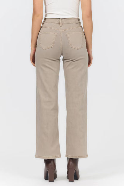 A person shown from the back wearing light beige straight-leg jeans with a white top and dark brown heeled boots, against a plain light gray studio background.