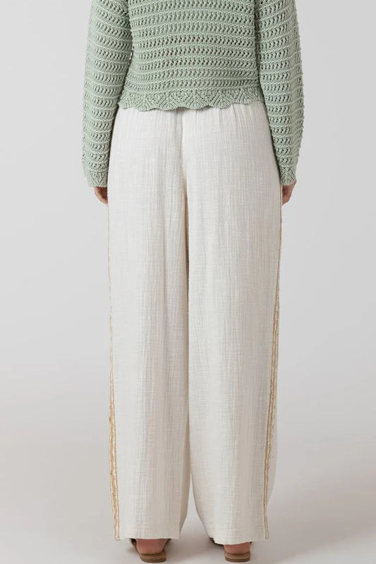 Person wearing a green textured sweater and white pants on a light gray background
