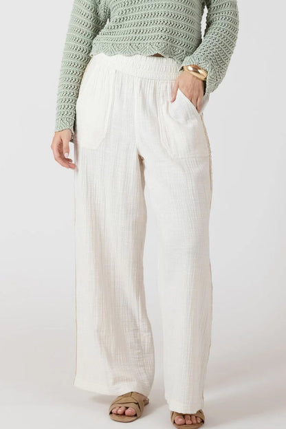 Person wearing a green sweater and white pants on a plain background