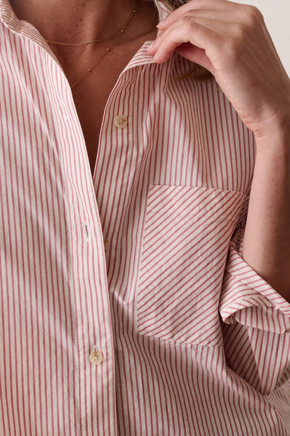 Close-up of a person wearing a pink and white vertically striped button-down shirt with rolled sleeves and a chest pocket, against a plain light background.