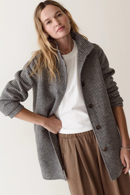 A woman modeling a gray and black houndstooth blazer over a white t-shirt and brown wide-leg pants, photographed against a solid off-white background.